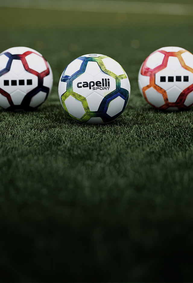 Three Capelli Sport Plasma soccer balls on a grass field, one with a visible brand logo.