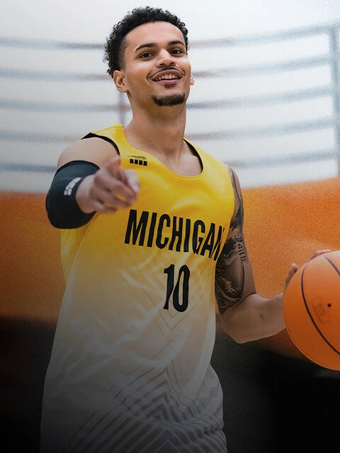 Person wearing a Capelli Sport Michigan basketball jersey holding a ball with a blurred background