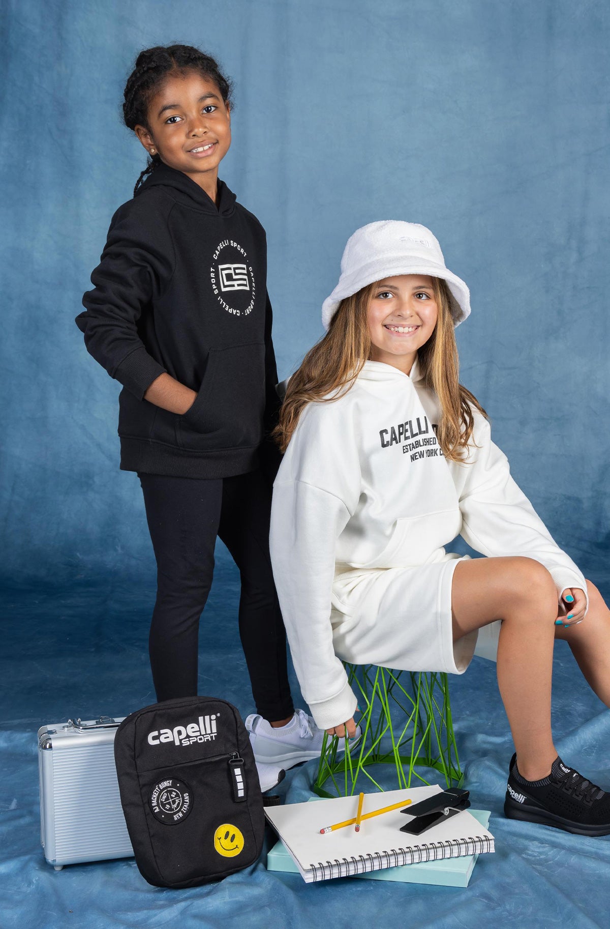 Two children in branded clothing with school supplies on a blue background.