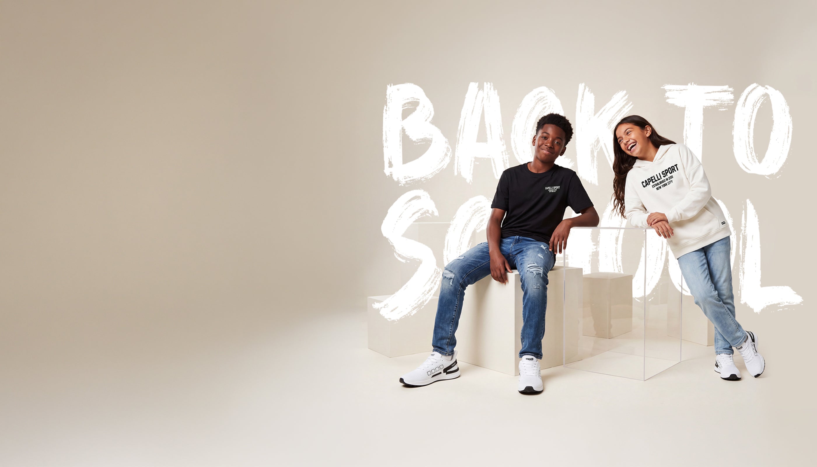Capelli Sport Back to School collection — two kids in Capelli Sport apparel: black graphic tee with jeans, and cream hoodie with jeans and sneakers.