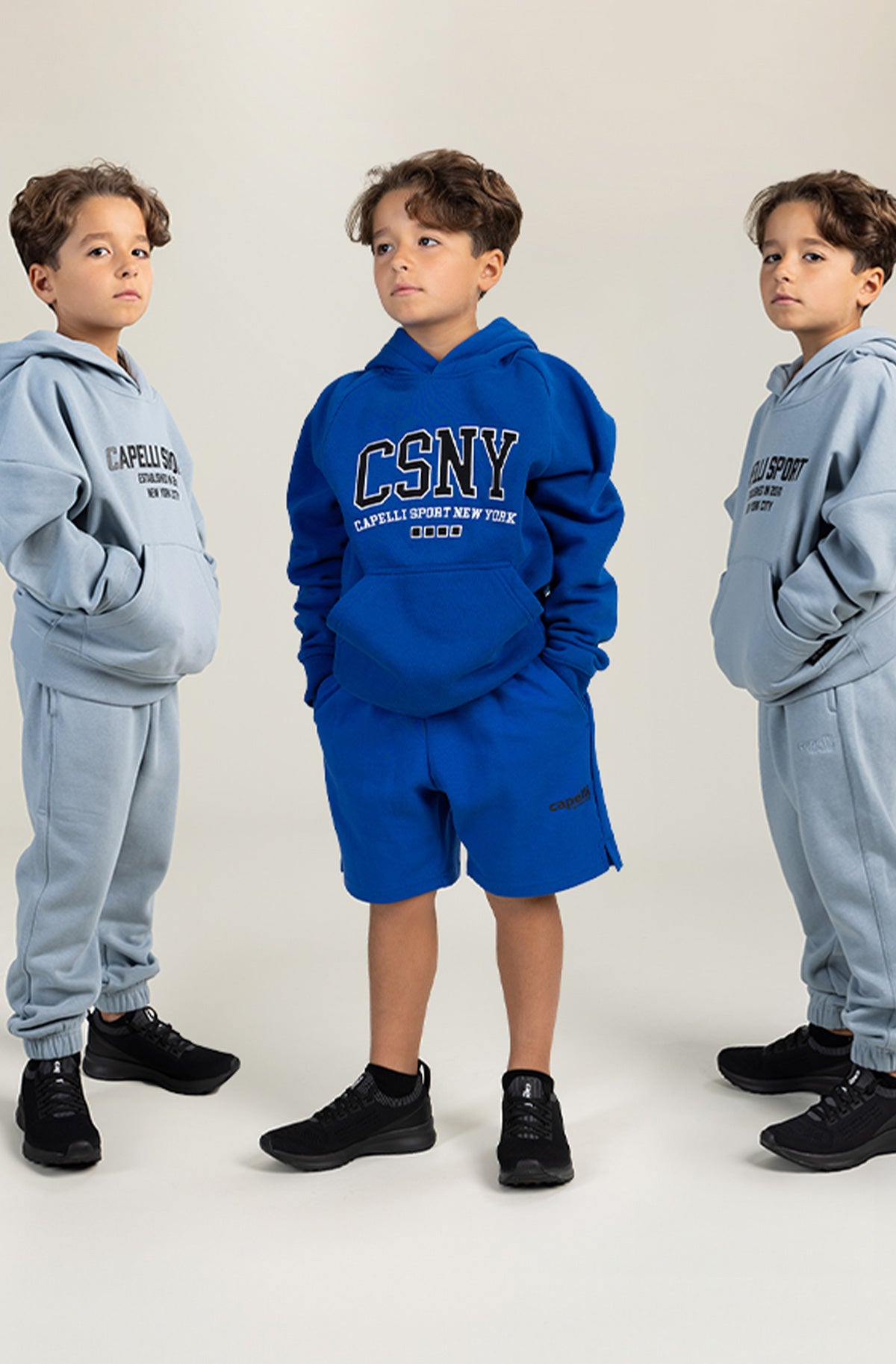 Three children wearing hooded sweatshirts in a row against a plain background
