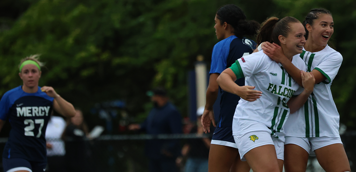 Three female soccer players in athletic uniforms celebrate on a field, with two in white and green Falcons jerseys hugging.
